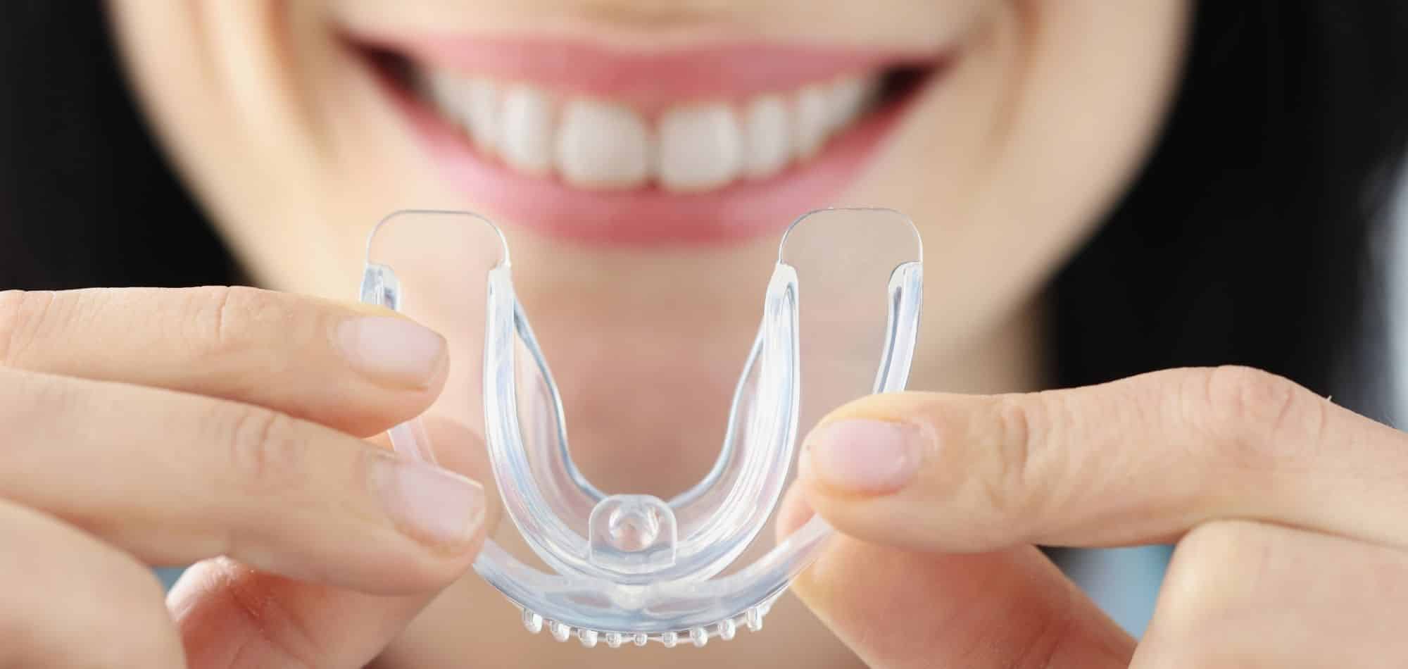 Smiling woman holding clear orthodontic retainer or aligner in front of teeth