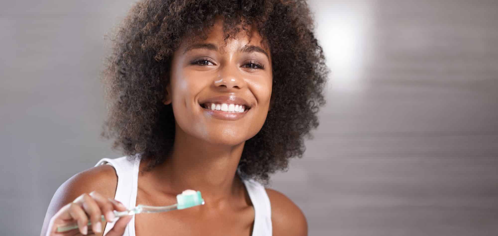 Smiling woman holding toothbrush in dental care setting against neutral background.