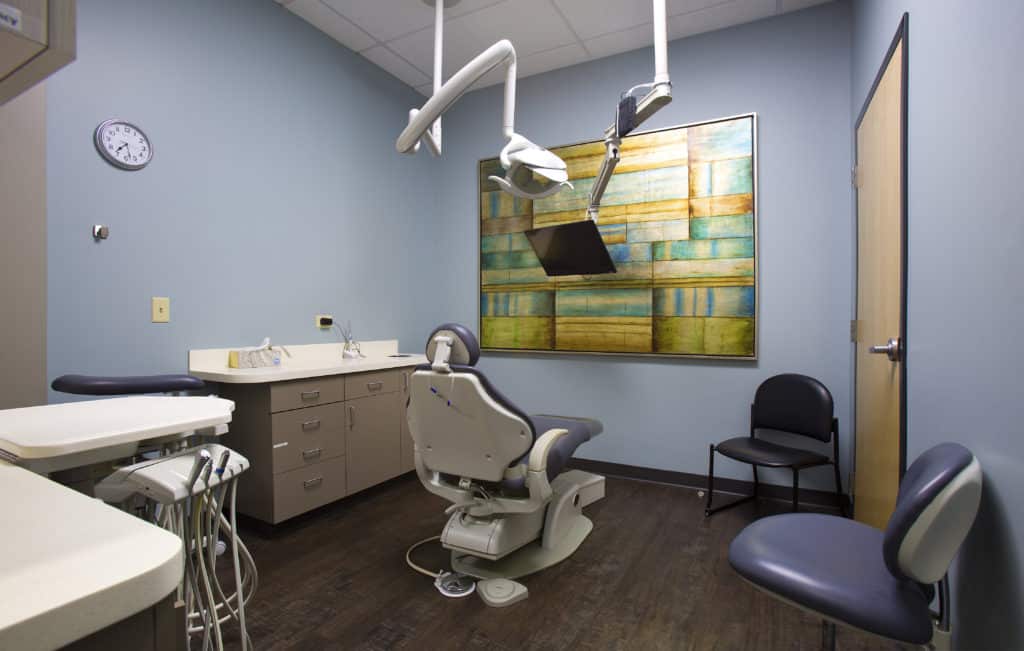 Modern dental operatory with chair, overhead lights, and treatment equipment in clinical setting.