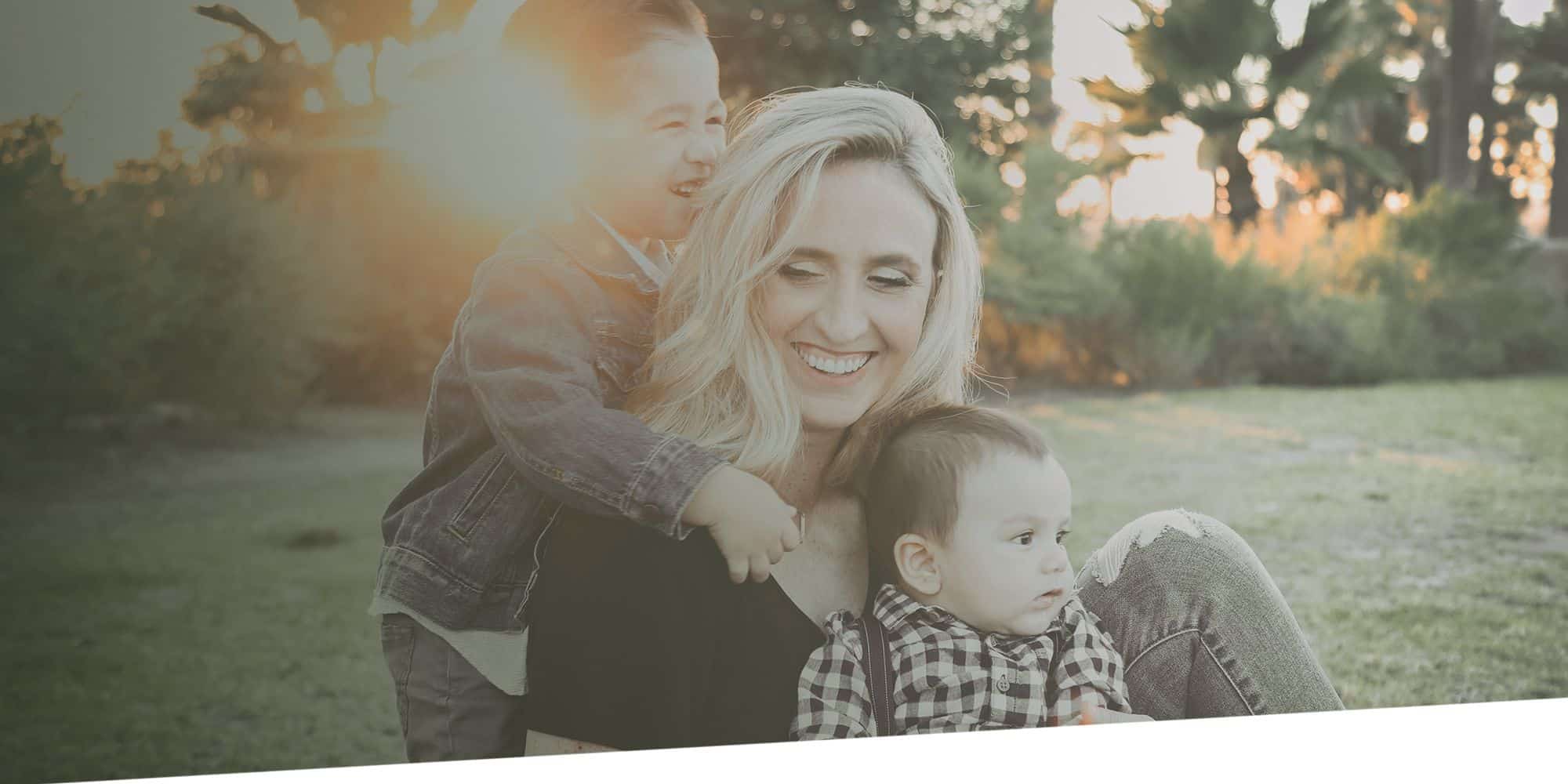 Woman and young child smiling outdoors at sunset in a natural setting.