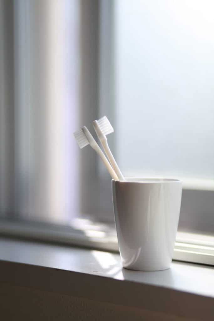Toothbrush in white cup on windowsill with natural light and curtains