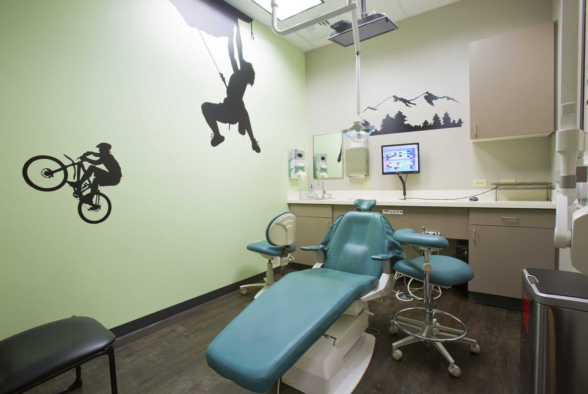 Dental examination room with blue chair, desk, computer, and extreme sports wall decals for pediatric patients.