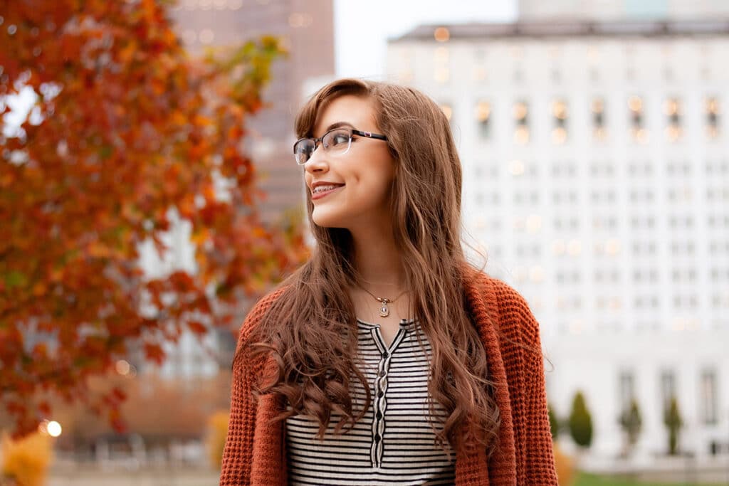 Woman wearing glasses and rust cardigan in autumn urban setting with fall foliage