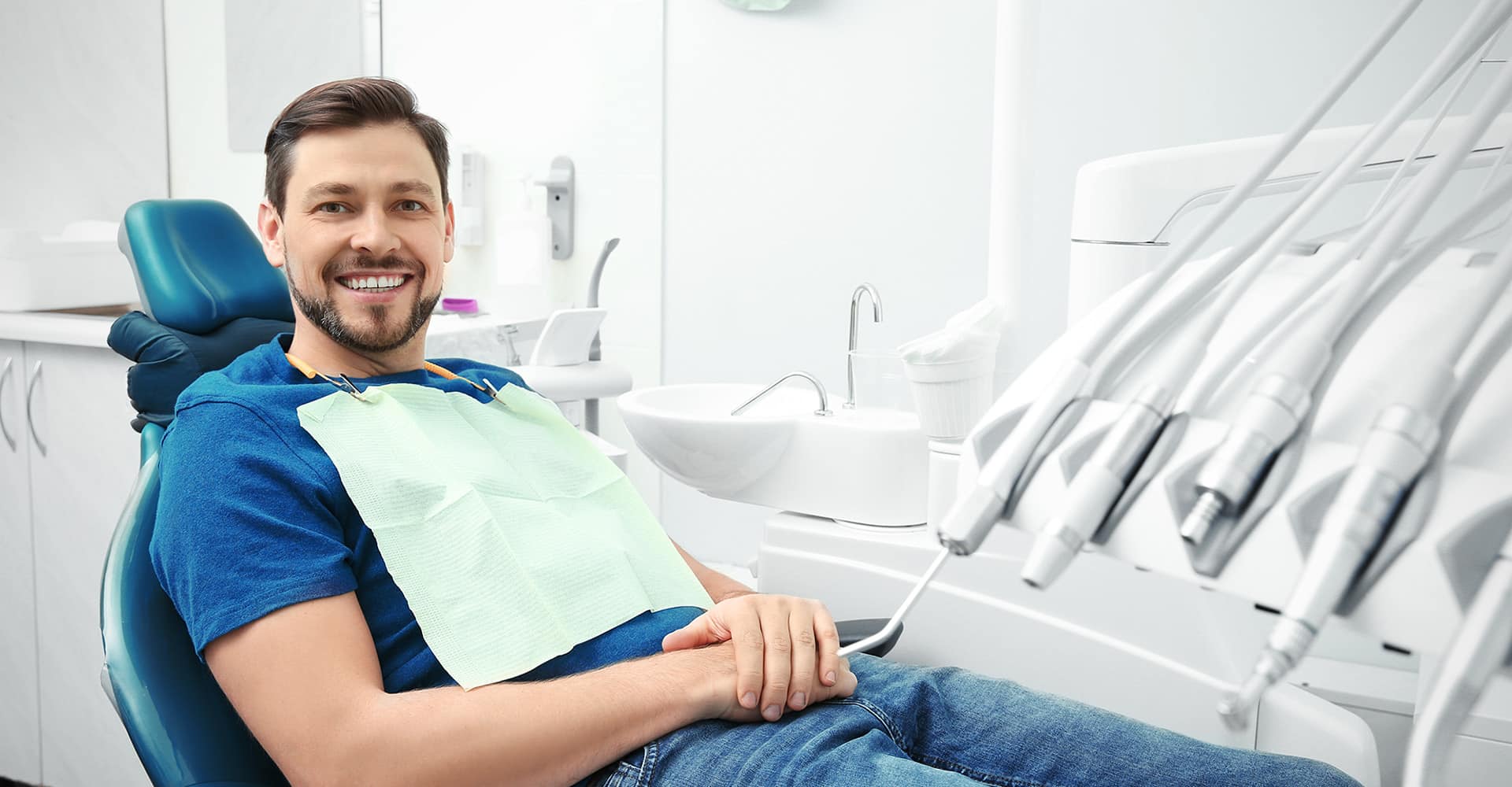 Male patient sitting in dental chair wearing bib in modern dental office.