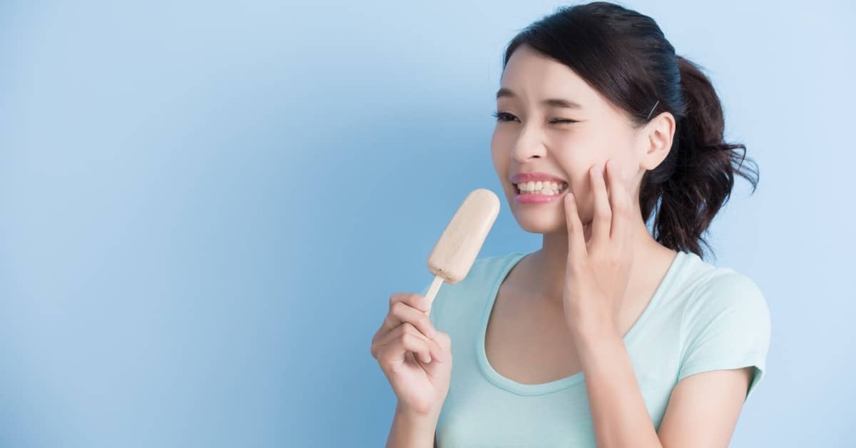 Woman holding ice cream cone against blue background, smiling brightly with hand near face.