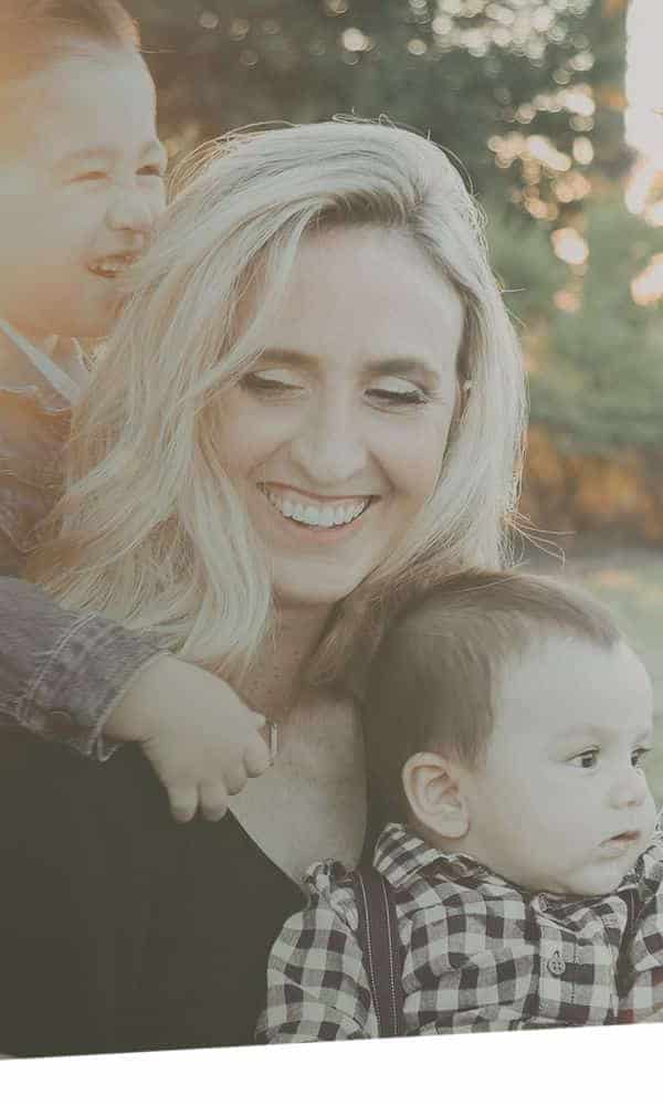 Family of three smiling together outdoors in warm, natural lighting.