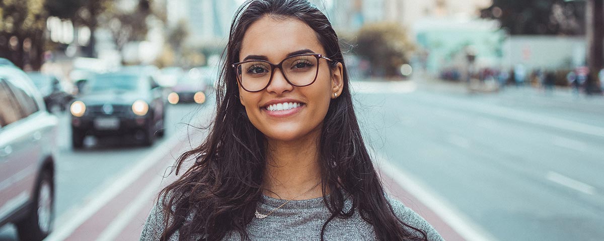 Young woman wearing glasses smiling on urban street with cars in background