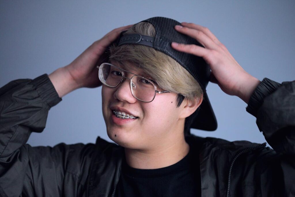 Young man wearing glasses and cap adjusting his hat against blue background.