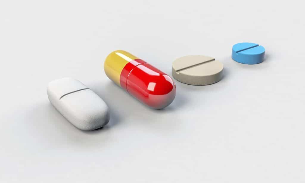 Four pharmaceutical pills and capsules arranged in a row on white surface.