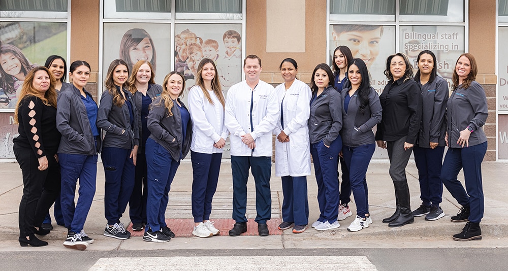 Dental team of professionals standing together in front of clinic building wearing uniforms.
