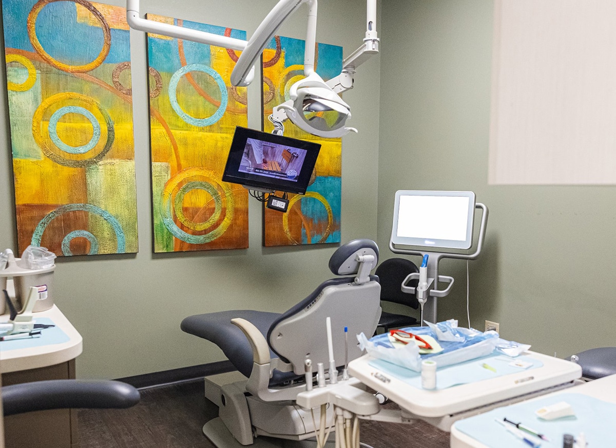 Modern dental operatory with chair, monitor, and colorful abstract artwork on walls.
