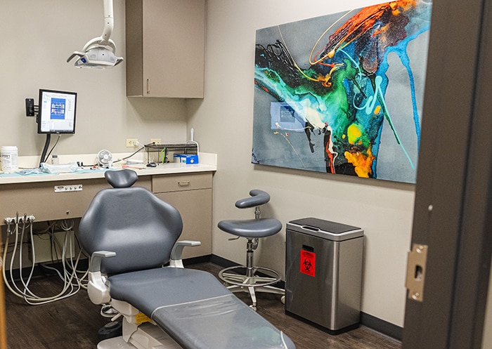 Modern dental operatory with treatment chair, overhead equipment, and digital display on wall.