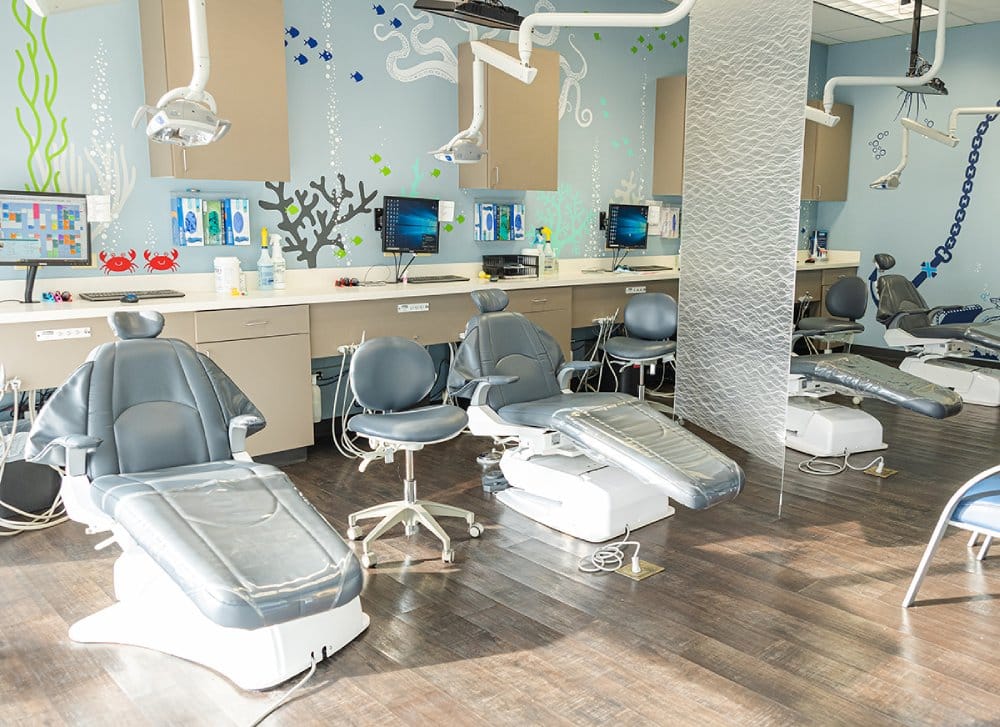 Modern dental office treatment area with chairs, overhead lights, and clinical equipment ready for patient care.
