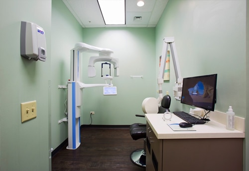 Modern dental examination room with green walls, computer workstation, and sterilization equipment.