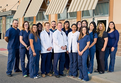 Dental team group portrait in blue and white scrubs standing outside clinic building.