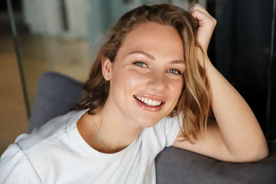 Young woman smiling at camera, wearing white t-shirt, casual indoor setting.
