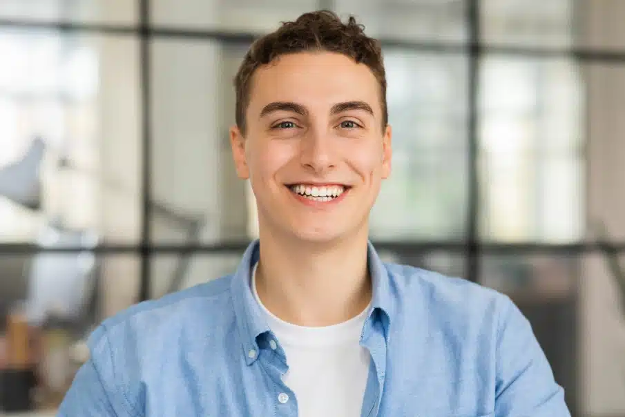 Young man smiling at camera in modern office setting wearing blue shirt