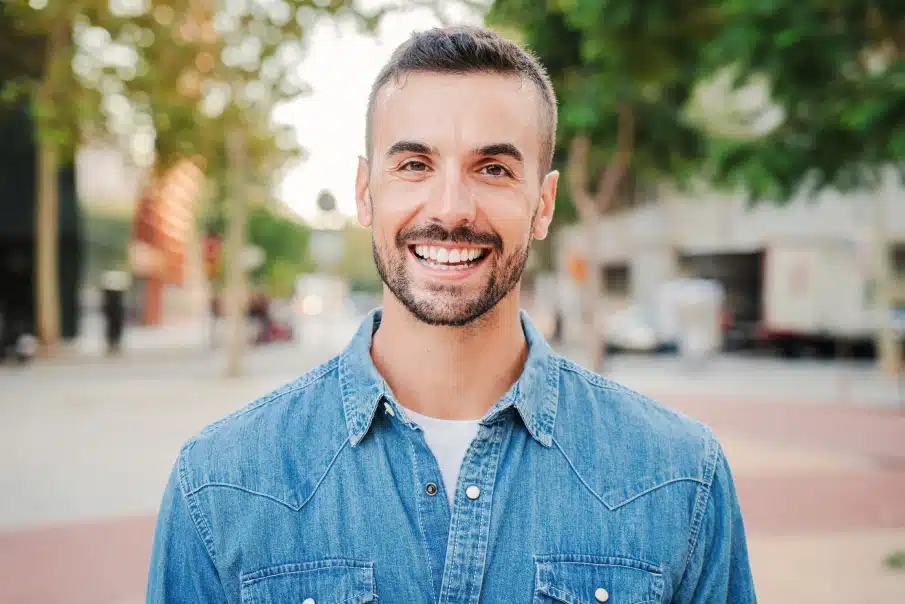 Smiling man in denim shirt outdoors on urban street during daytime.