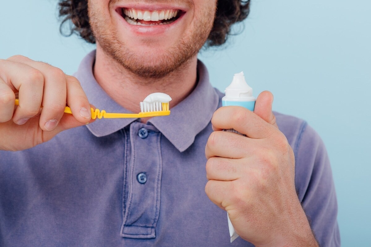 Man holding yellow toothbrush with toothpaste smiling, demonstrating proper oral hygiene after composite filling at Denver d.