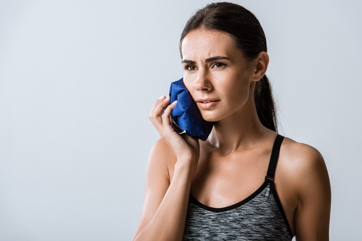 Woman holding ice pack to cheek for emergency dental pain relief in Denver, CO.